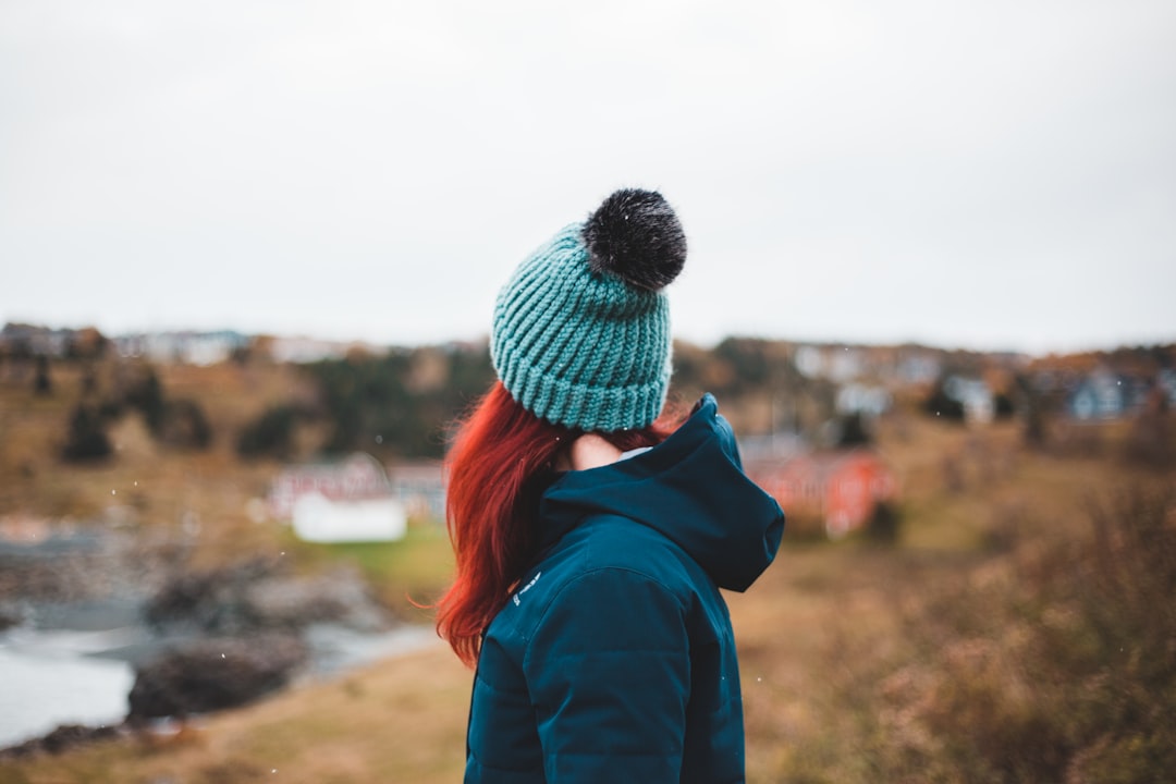 woman in blue jacket and gray knit cap standing on brown field during daytime