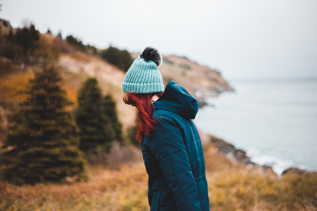 person in blue jacket and white knit cap standing on brown grass field during daytime