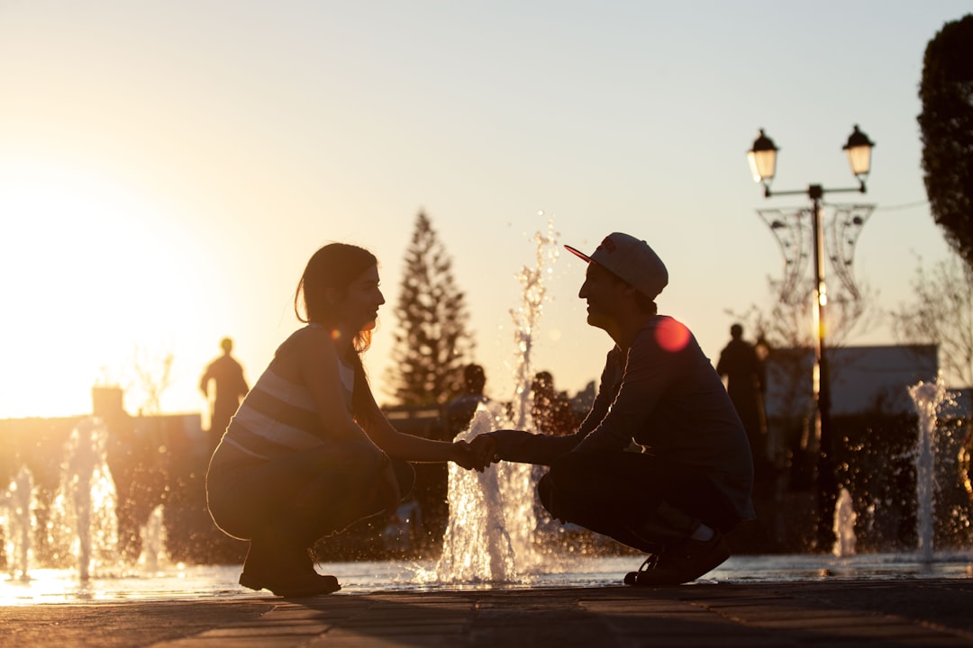 man and woman sitting on water fountain during sunset