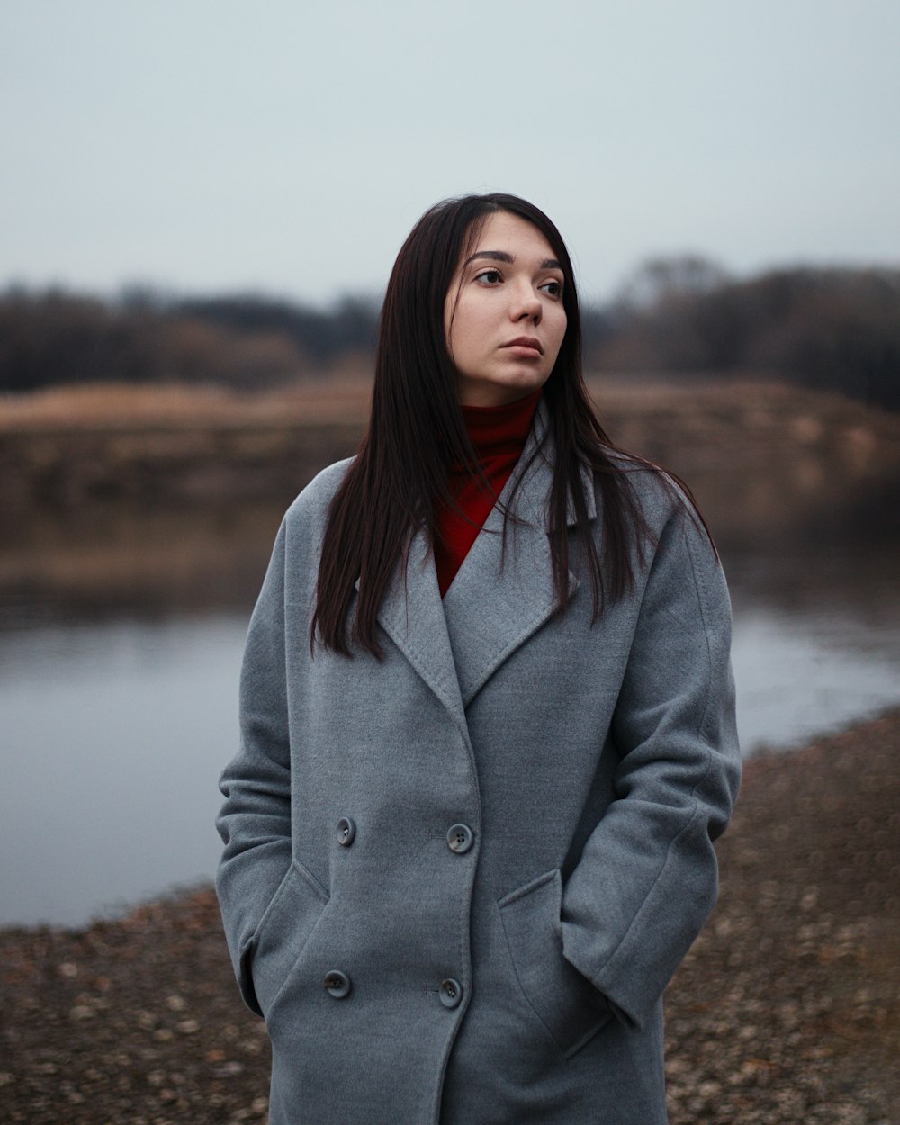 woman in gray coat standing near lake during daytime