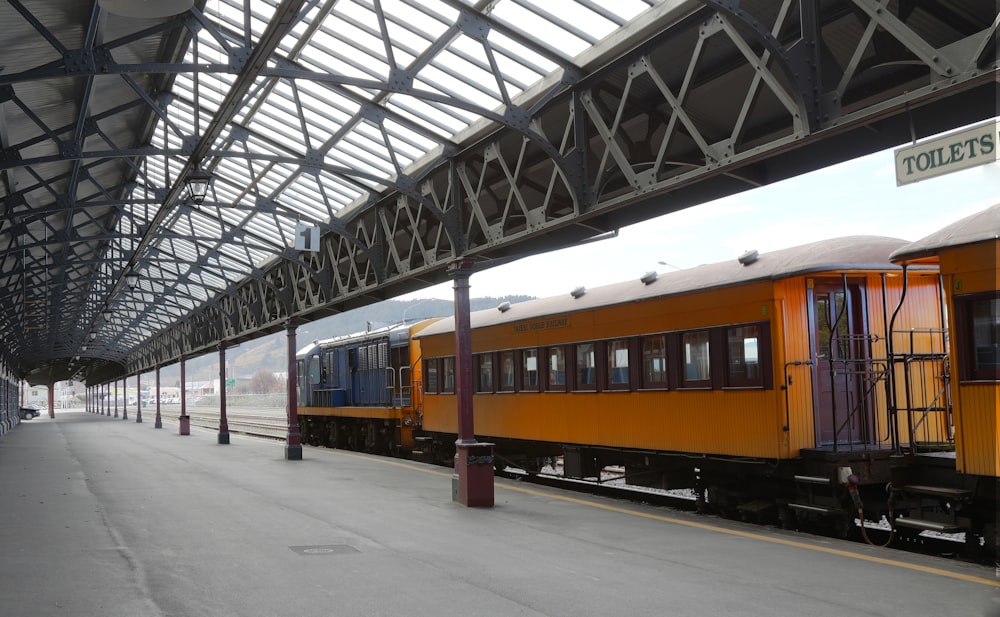 yellow and black train on rail tracks under gray metal bridge
