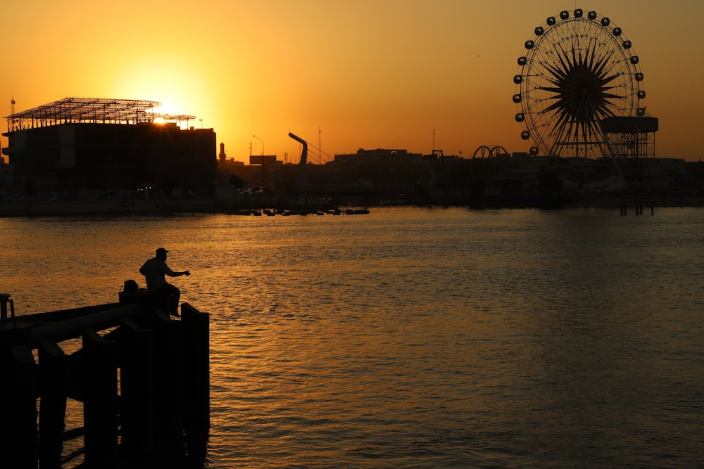 silhouette de personne assise sur un banc près de la grande roue pendant le coucher du soleil