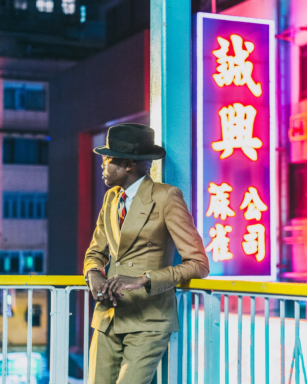 man in brown coat wearing black hat standing near red and yellow wall