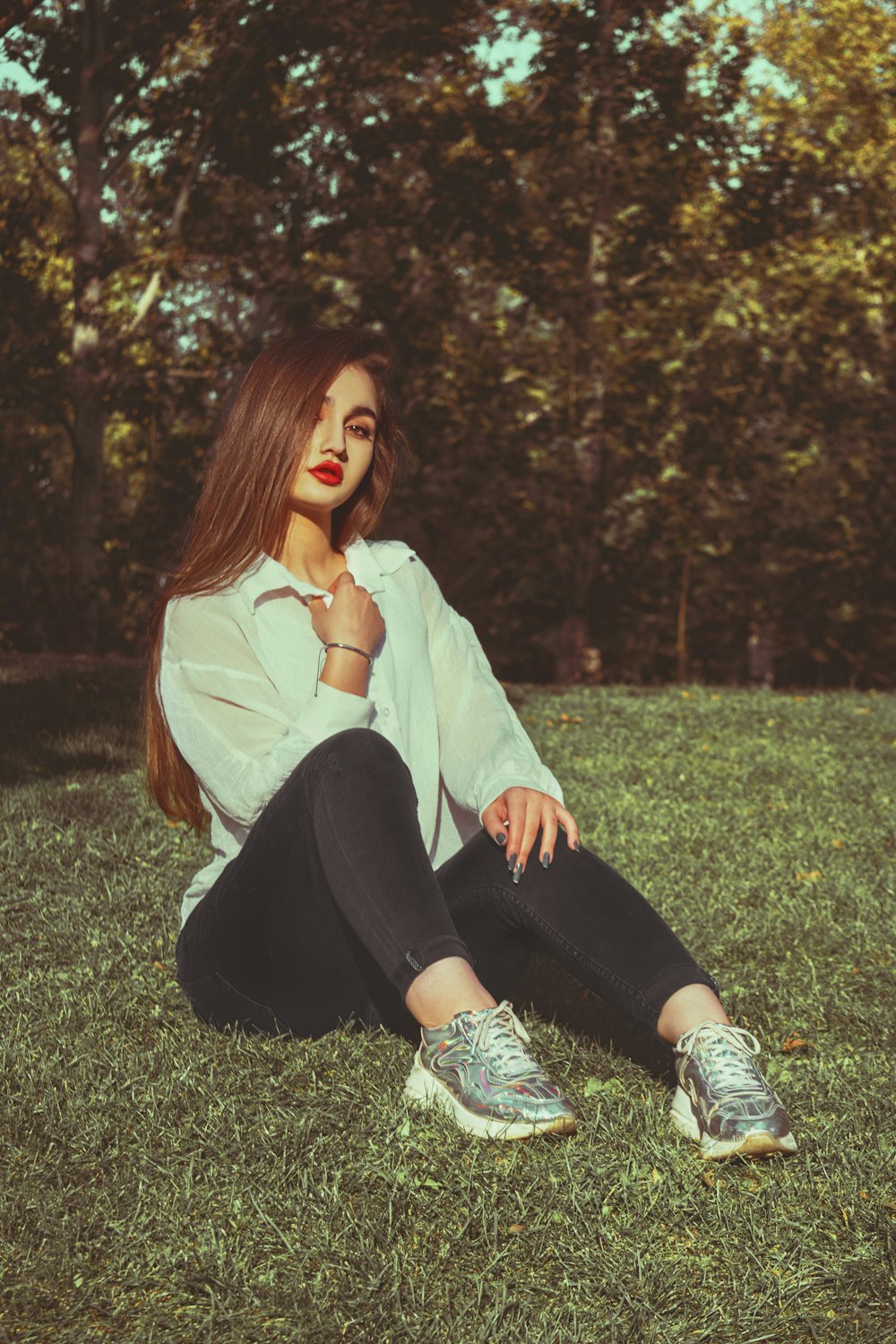 woman in white long sleeve shirt and black pants sitting on green grass field during daytime