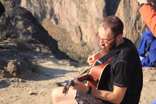 The musician playing an acoustic guitar by a scenic mountain backdrop.