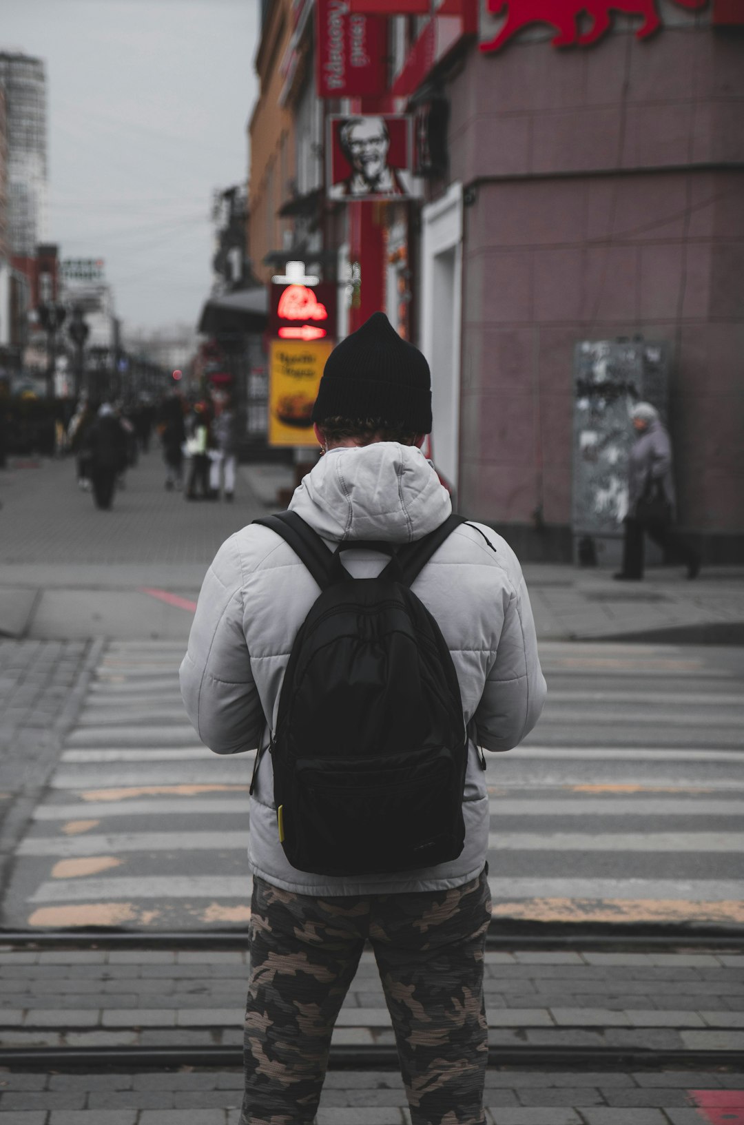 man in white shirt and black backpack walking on pedestrian lane during daytime