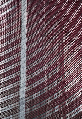 Steel and glass building facade with red horizontal slats creating a dynamic, modern architectural design.