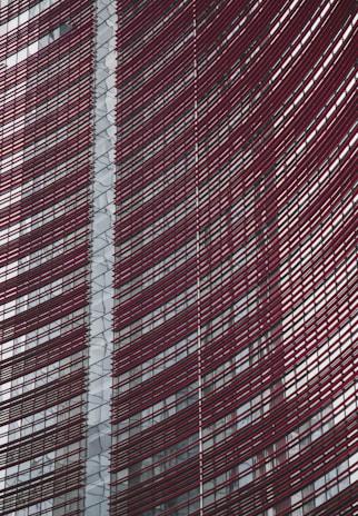 Steel and glass building facade with red horizontal slats creating a dynamic, modern architectural design.