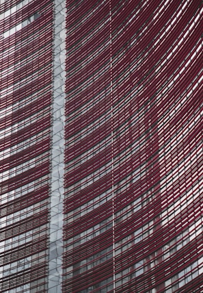 Steel and glass building facade with red horizontal slats creating a dynamic, modern architectural design.