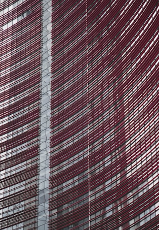 Steel and glass building facade with red horizontal slats creating a dynamic, modern architectural design.