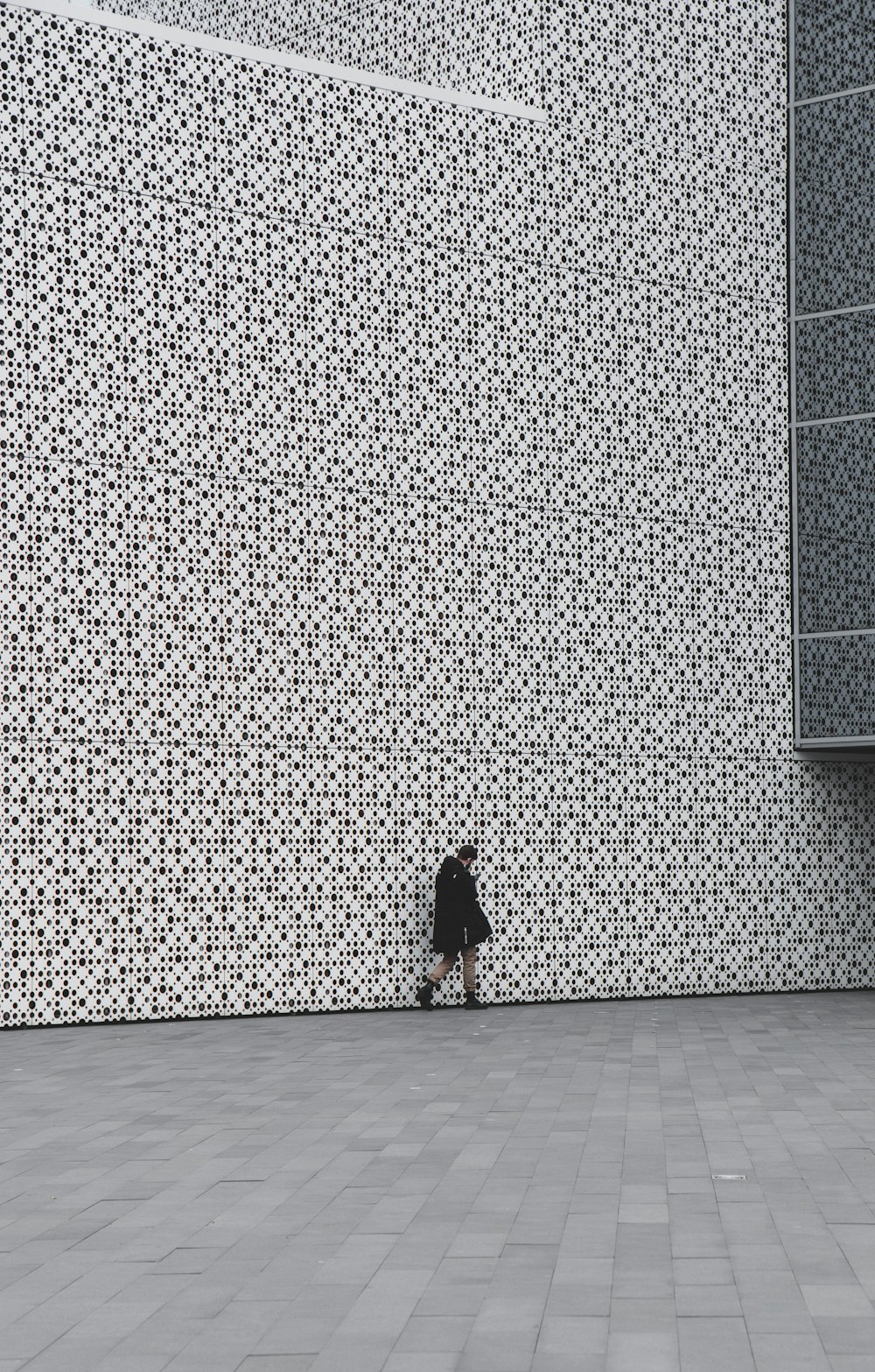 Person im schwarzen Mantel steht an grauer Wand