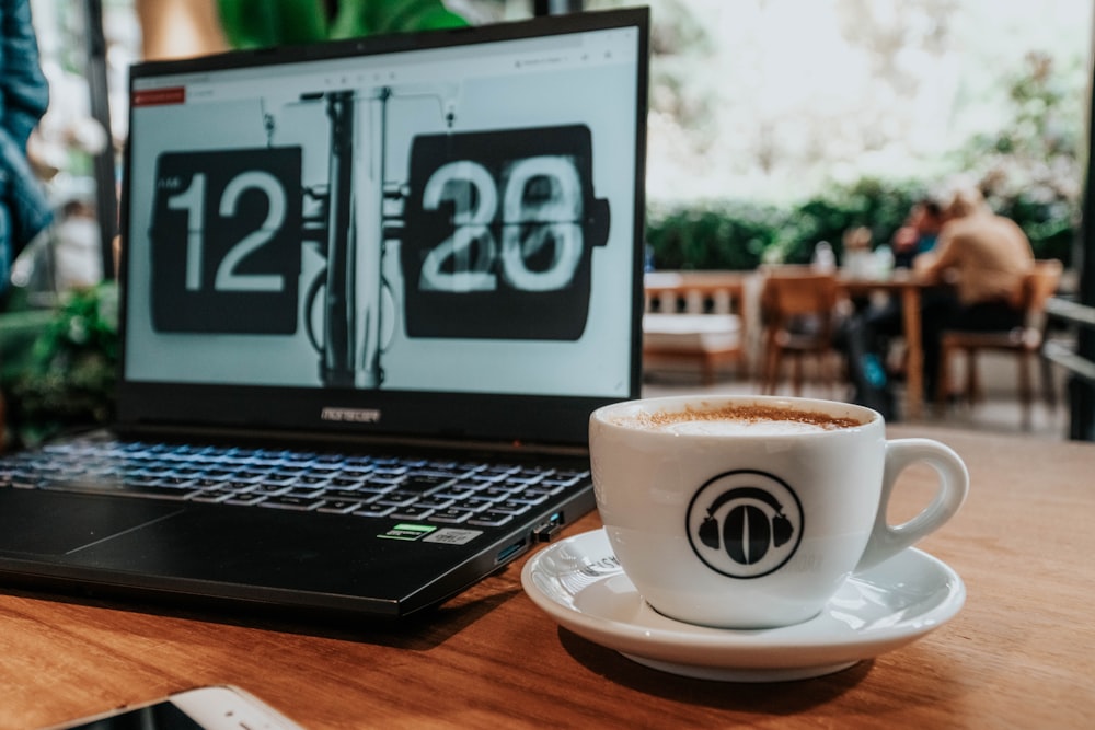 black and silver laptop computer beside white ceramic mug with saucer on brown wooden table