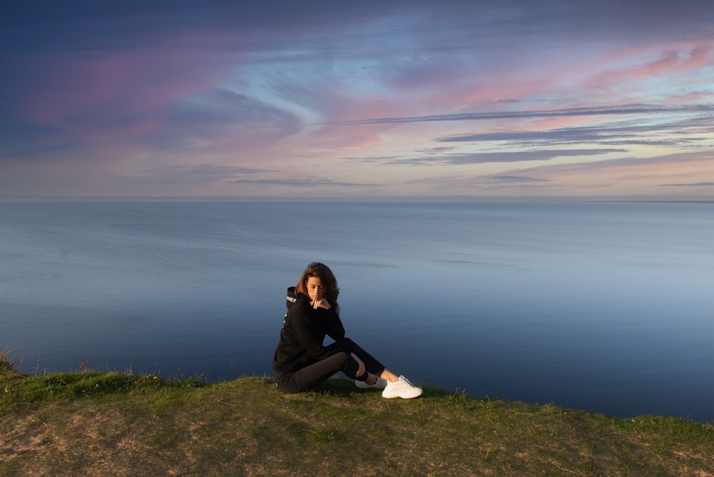 woman in black jacket sitting on green grass field