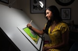 A woman artist is drawing at a drafting table.
