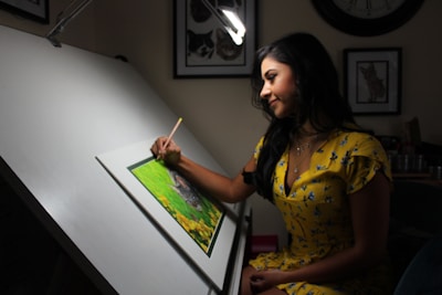 A woman artist is drawing at a drafting table.
