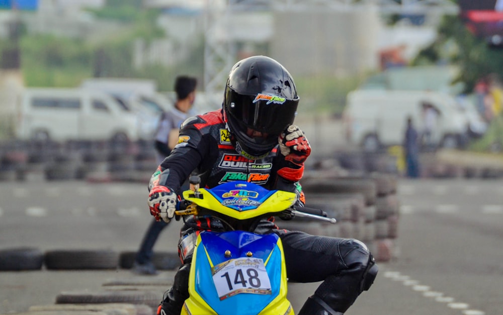 man in black jacket riding yellow and blue sports bike