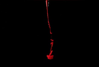 A stream of bright red liquid is flowing down through a dark black background, creating an abstract, dramatic effect.