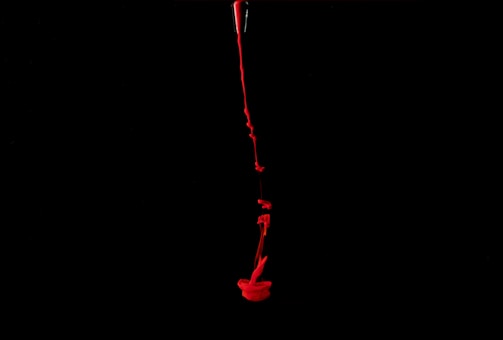 A stream of bright red liquid is flowing down through a dark black background, creating an abstract, dramatic effect.