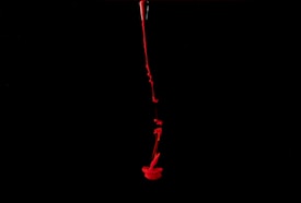 A stream of bright red liquid is flowing down through a dark black background, creating an abstract, dramatic effect.