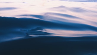 Gentle ripples on a glassy lake at dawn, framed by soft mist and distant hills.