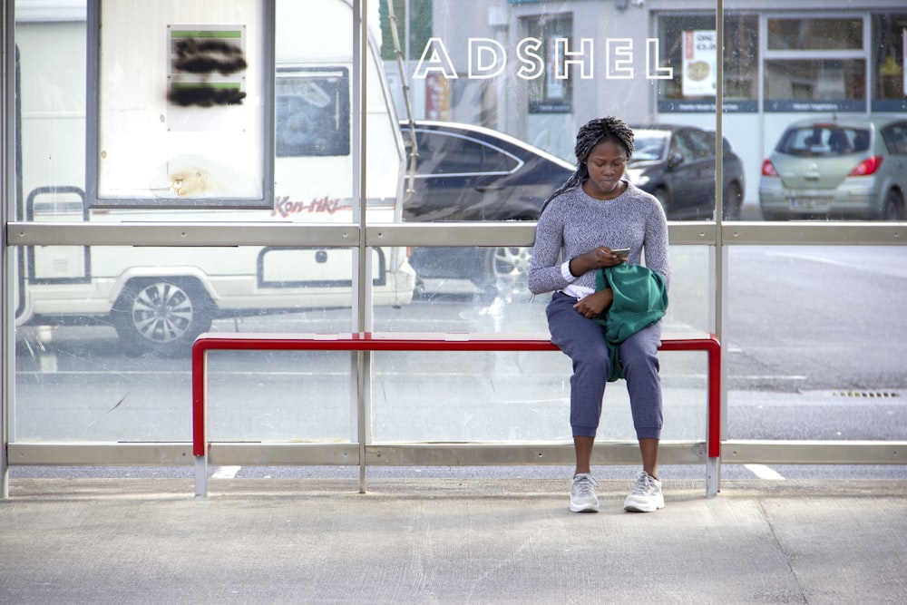 Mujer con camisa gris de manga larga y jeans de mezclilla azul sentada en una silla roja