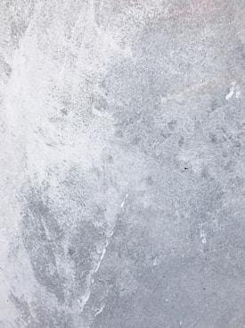 A textured grey surface with subtle variations in shading and patterns, resembling concrete or a rough wall finish.