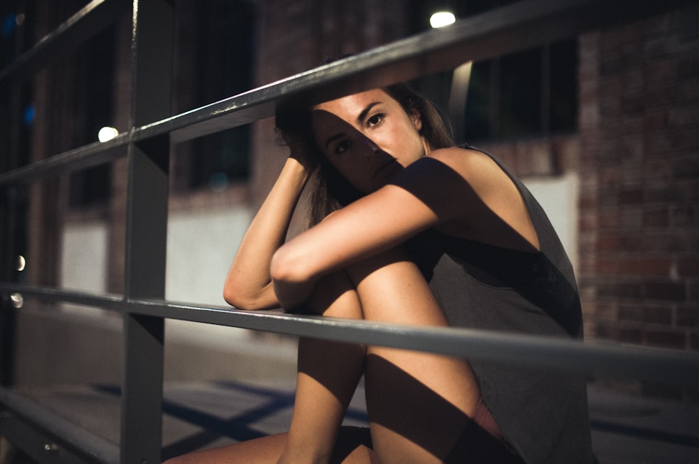 a woman is sitting on a fence with her hands on her head