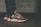 A close-up view of a person wearing stylish sneakers with a striking design, combining dark blue, red, and white colors. The shoes have a textured, thick sole and patterned laces. The person is wearing dark jeans, and the background features a tiled wall with a muted color scheme.