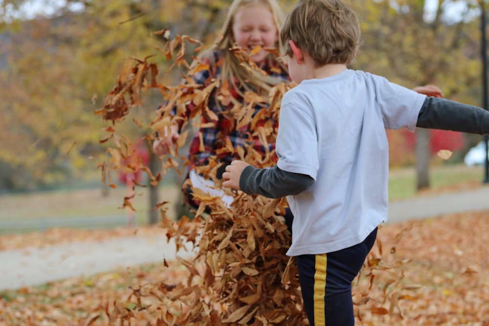 boy in white long sleeve shirt and yellow and black striped pants standing on dried leaves