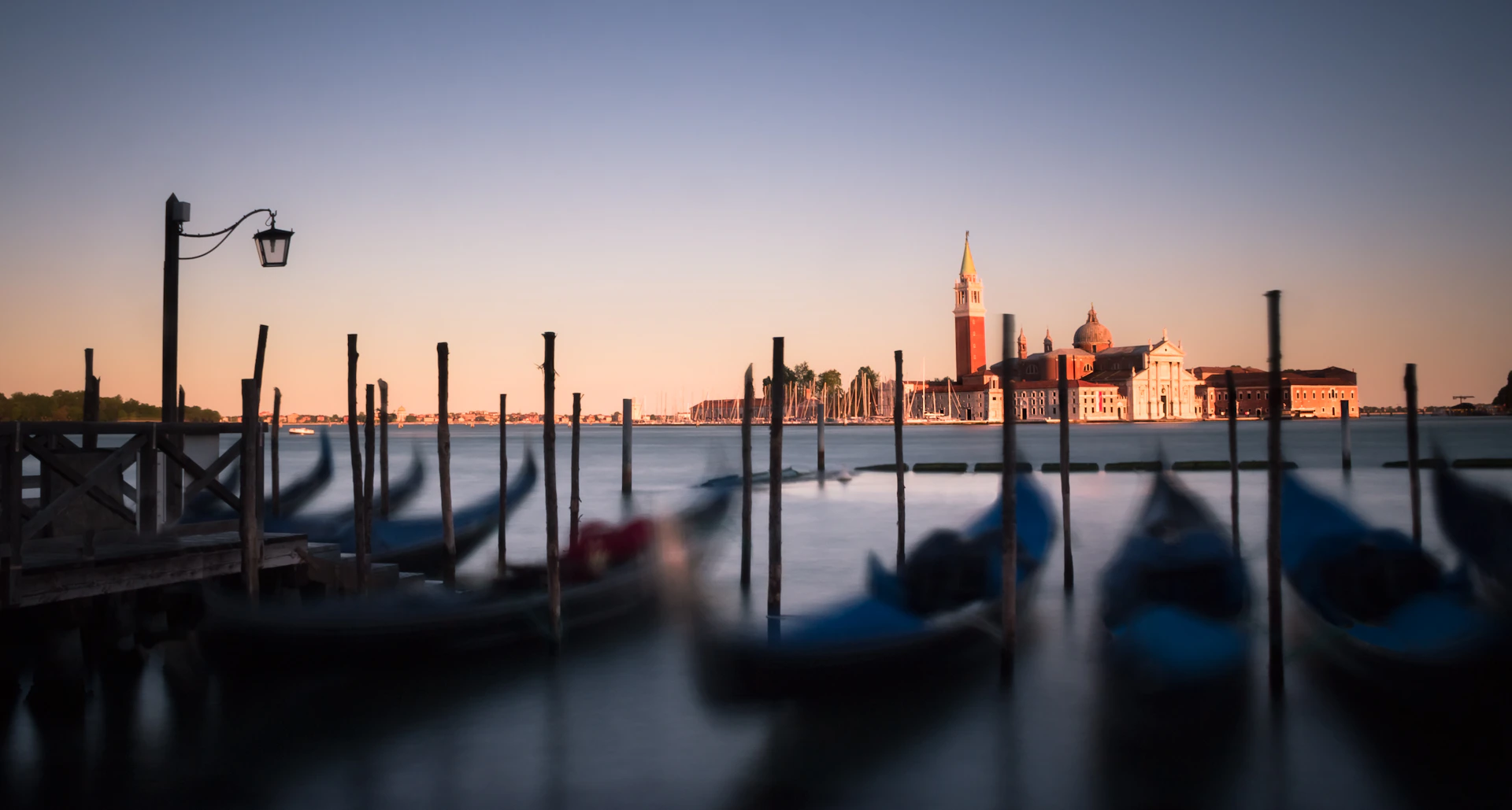 A serene view of Venice's canals at sunrise, with gondolas gently floating on the water.