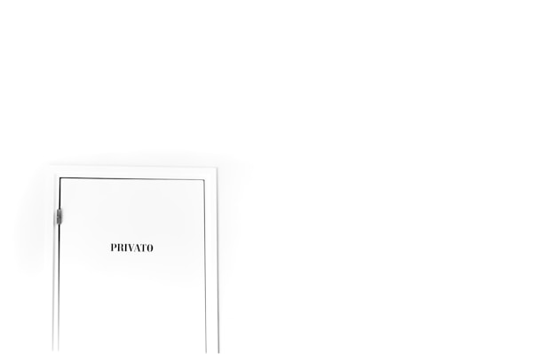A white door is set against an almost entirely white wall, positioned in the lower left corner. The door has the word 'PRIVATO' written on it, indicating restricted access or privacy.