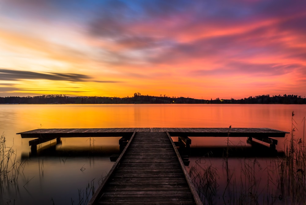 Muelle de madera marrón en el lago durante la puesta del sol