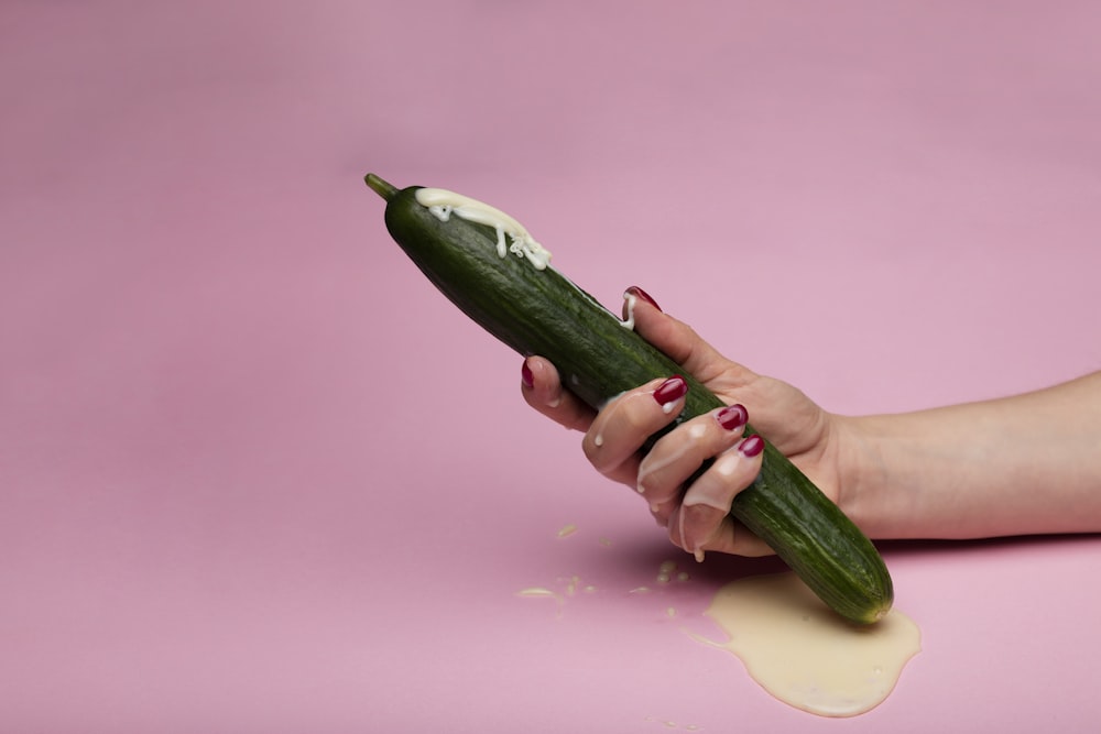 person holding green cucumber on pink surface
