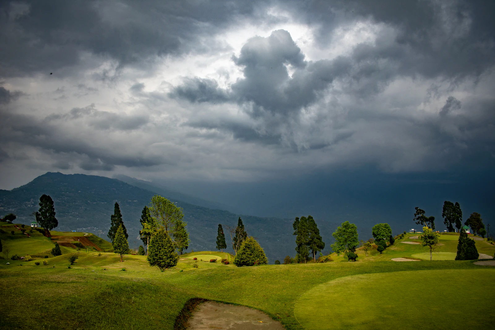 Storm clouds gathering over the grassy golf greens and pines on Deolo hill above Kalimpong
