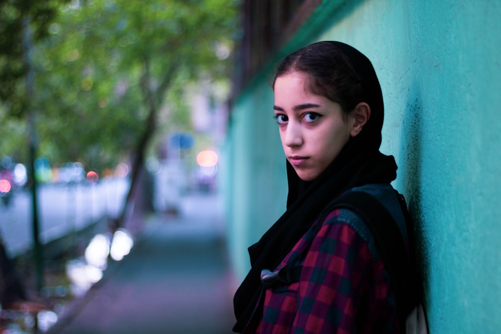 woman in red and black plaid scarf standing near green wall during daytime