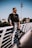 man in black and white long sleeve shirt and blue denim jeans sitting on white wooden