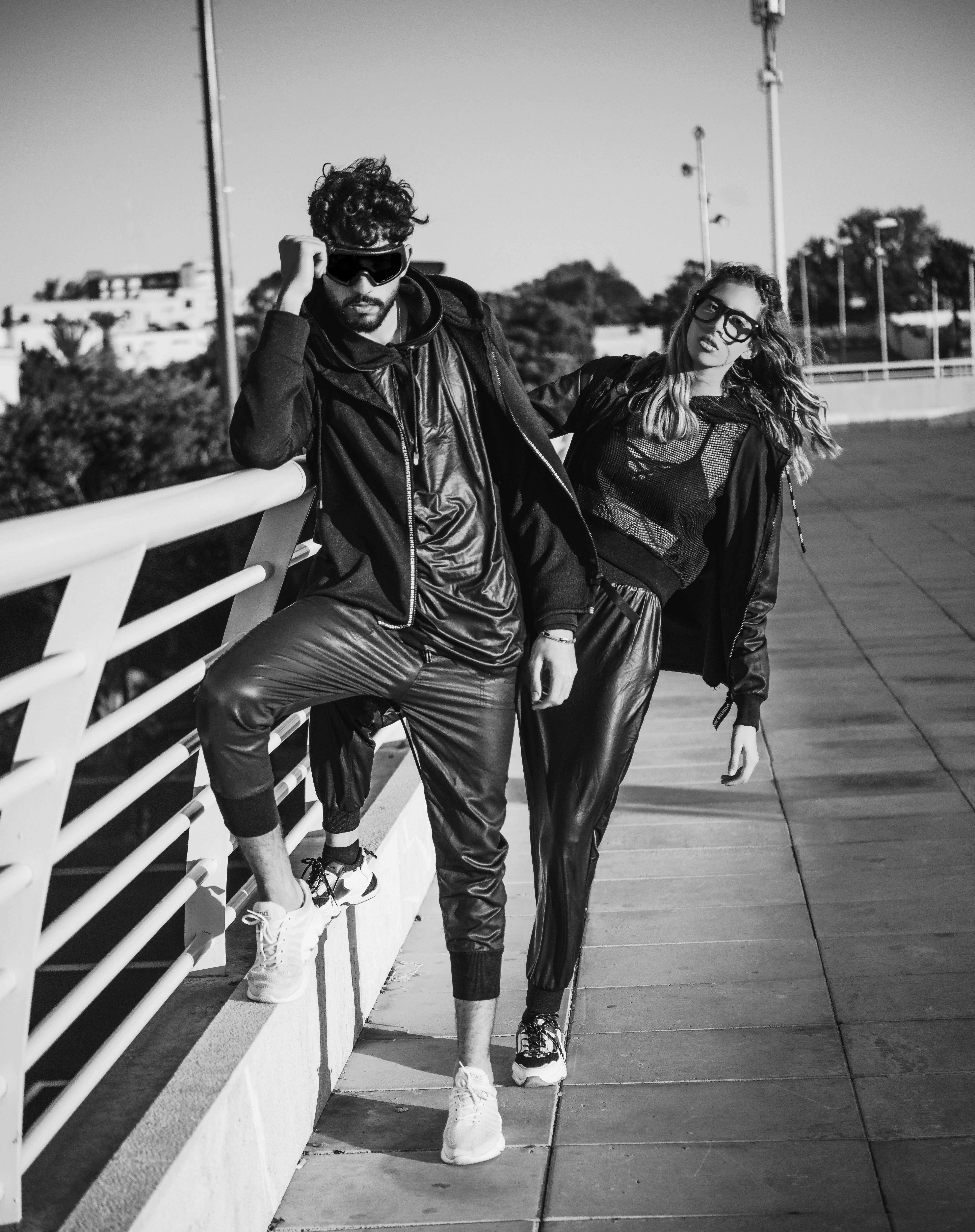 Two people wearing dark clothing pose by a white railing.