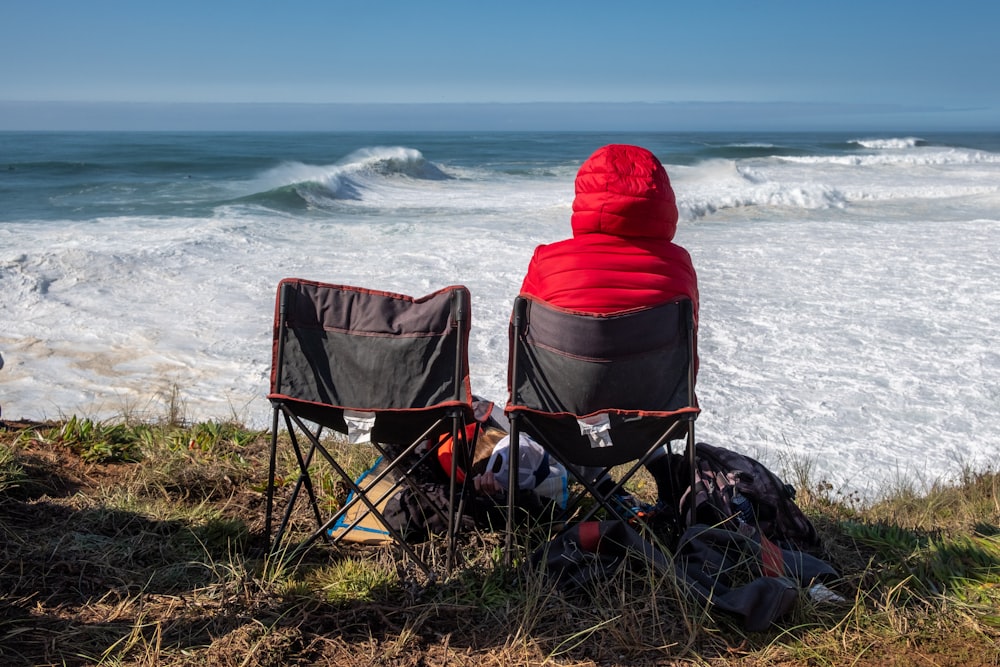 personne en sweat à capuche rouge assis sur une chaise de camping bleue au bord de la mer pendant la journée