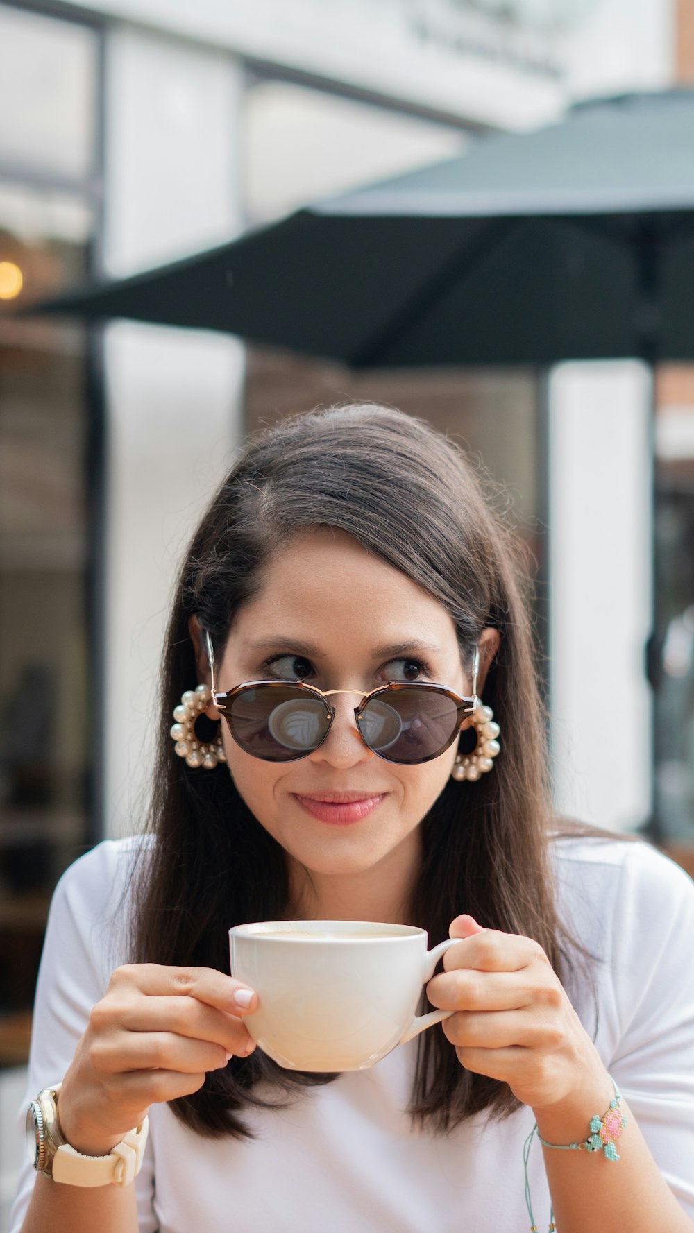 woman in white shirt wearing brown sunglasses holding white ceramic mug