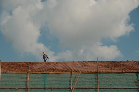 Close-up of a construction worker fixing a damaged commercial roof under bright blue skies.