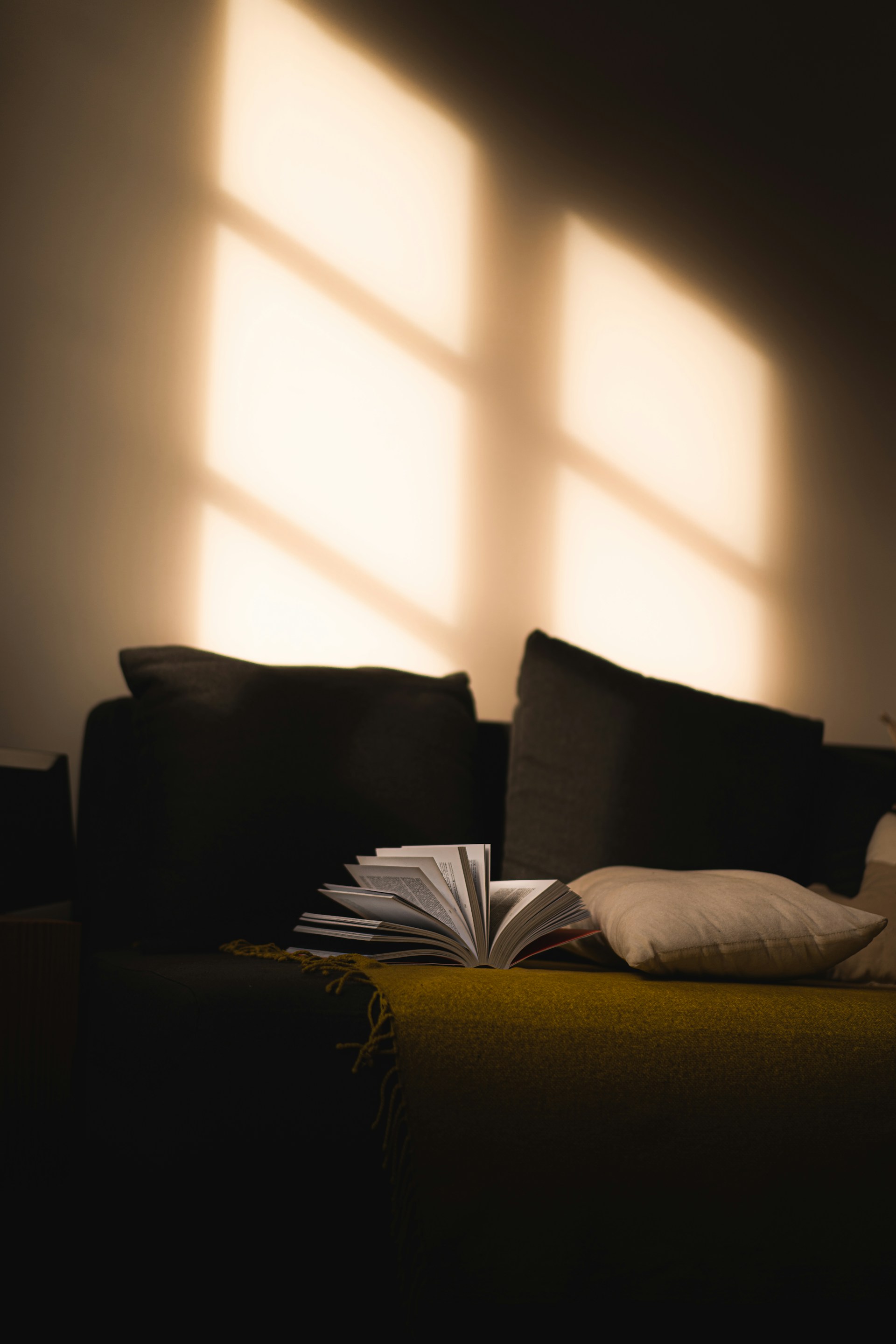 A cozy living room scene featuring a soft, oversized bean bag sofa with a person reading a book, sunlight streaming through a nearby window.
