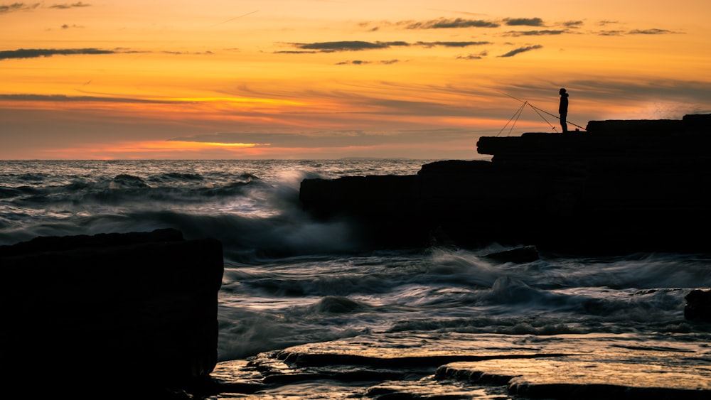 silhouette of rock formation on sea during sunset