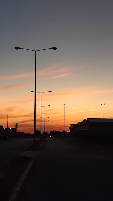 Installation team setting up LED streetlights along a quiet town road during sunset