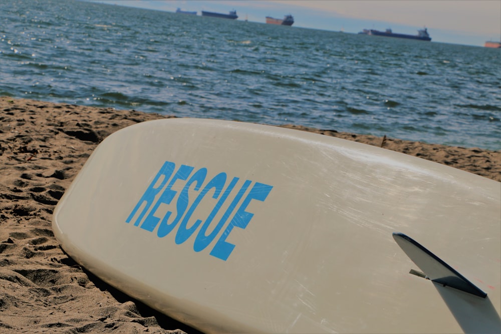 Tabla de surf blanca y azul sobre arena marrón cerca del cuerpo de agua durante el día