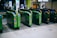 Several automatic ticket gates are lined up at a train station entrance, predominantly green in color with visible IC card slots and directional arrows. In the background, there are posters on the walls and a few people walking past.