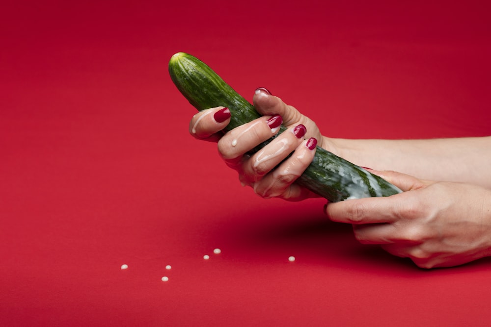 person holding green cucumber on red table