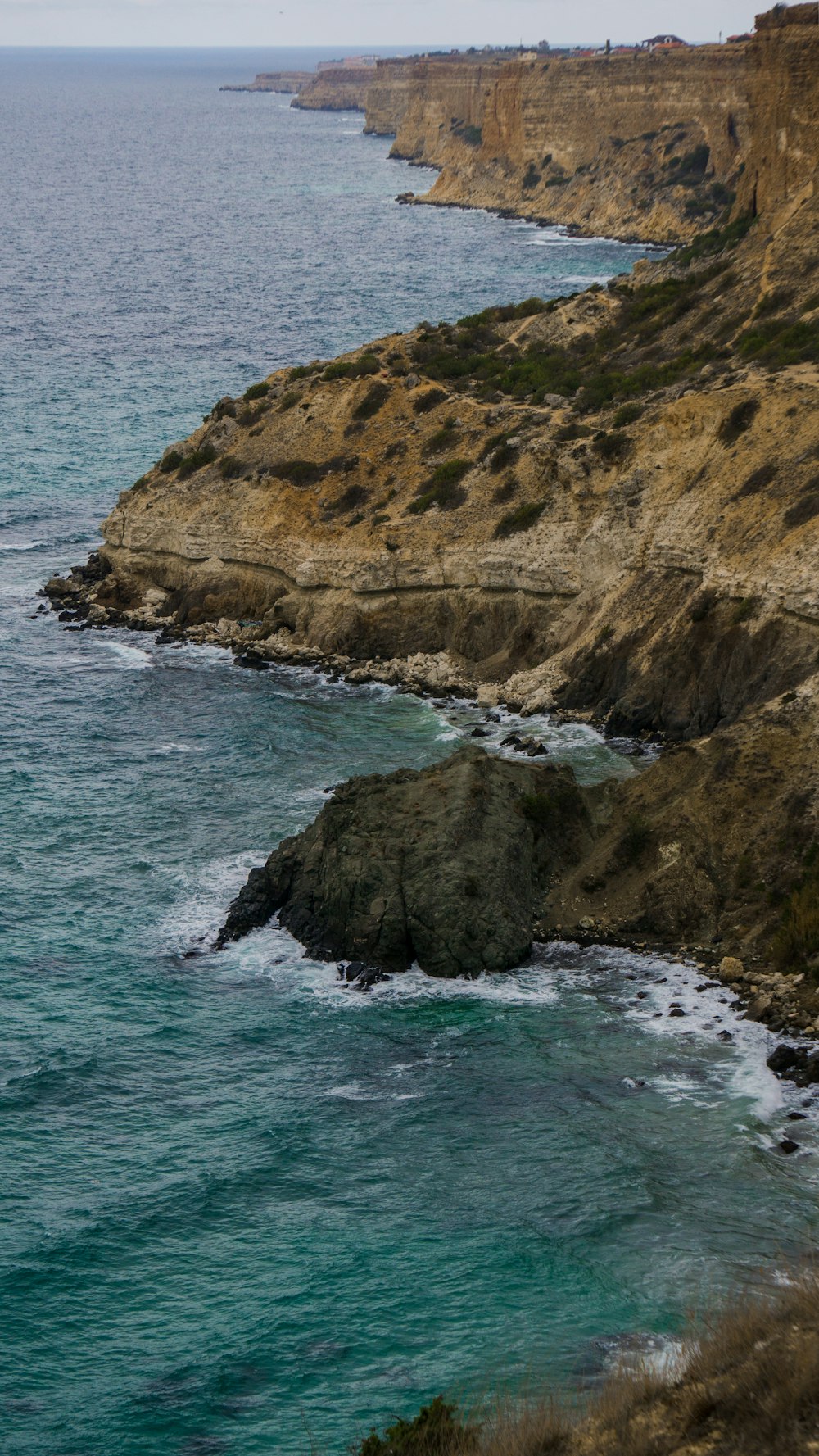 brown and green rock formation beside body of water during daytime