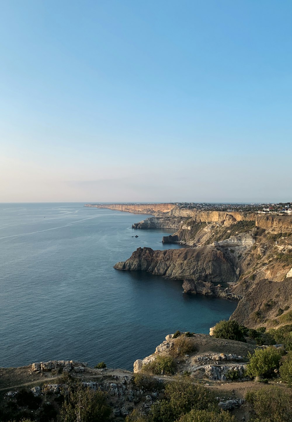 Braune und grüne Klippe am Meer unter blauem Himmel tagsüber