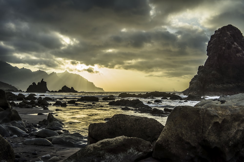 rocky shore with rocks and mountains in the distance under grey cloudy sky