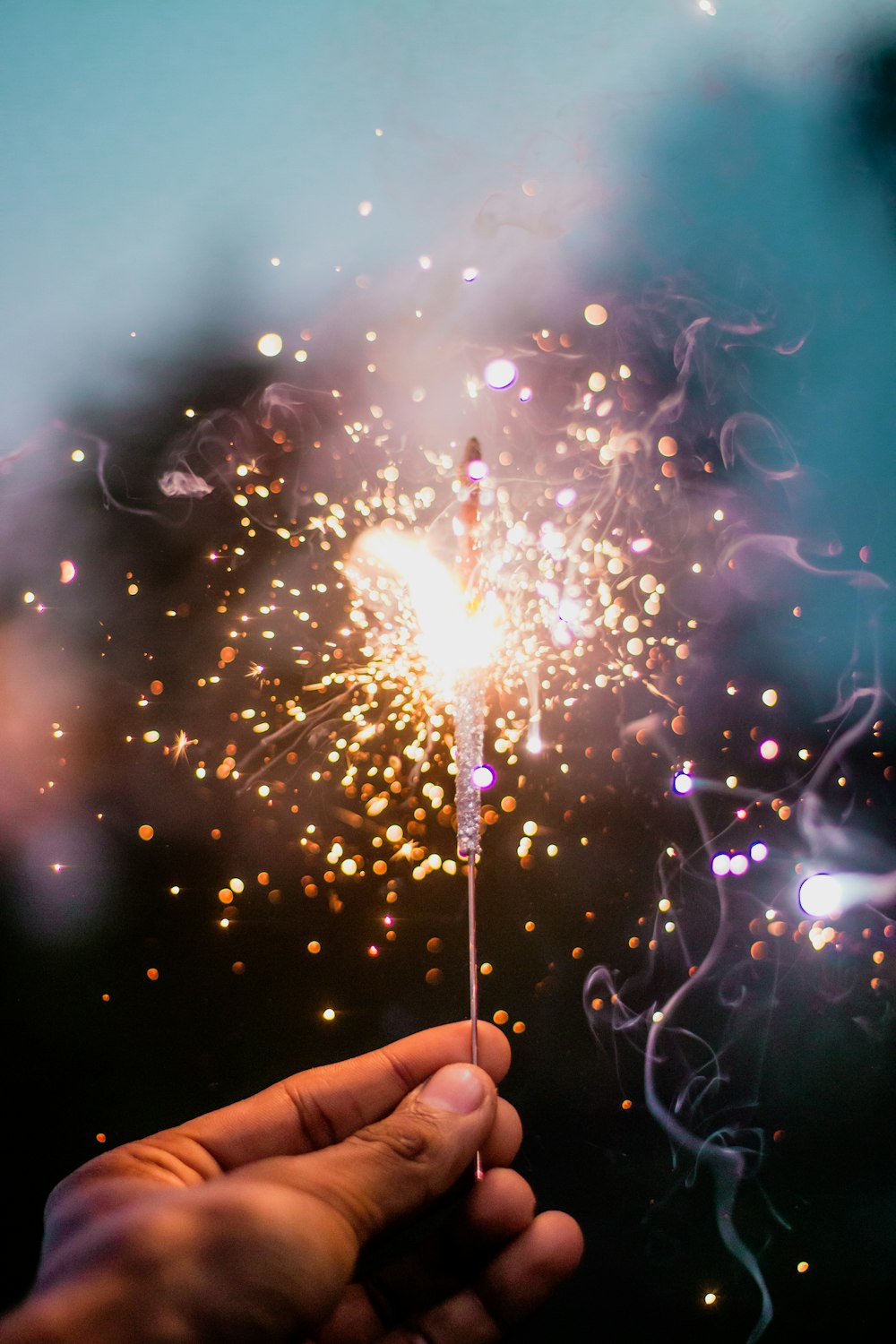 person holding lighted sparkler with lights